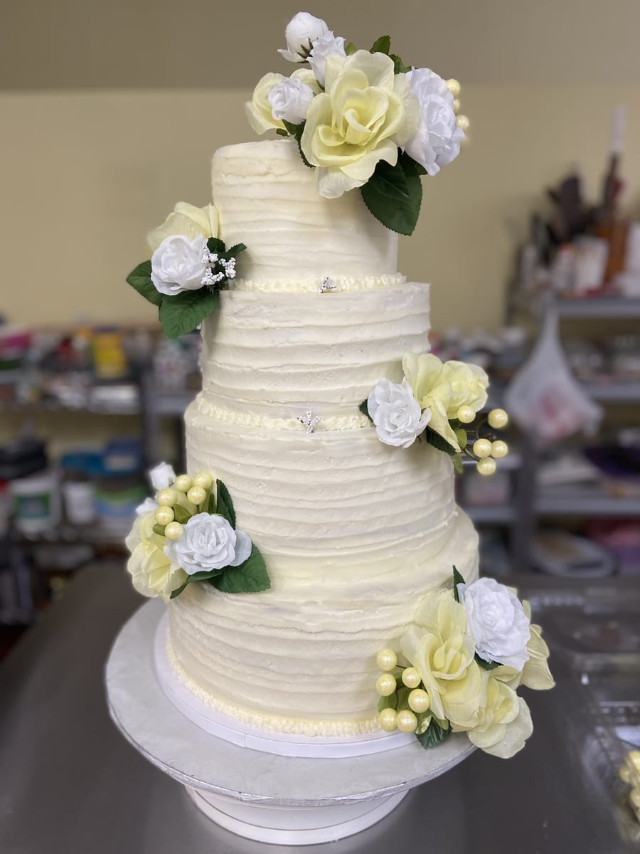 A Cakes Castle wedding cake photographed on a phone in the bakery, with a cluttered background